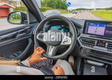 Vue rapprochée de la femme conducteur conduisant la nouvelle BMW iX3 M Sport voiture noire modèle électrique sur l'autoroute. Banque D'Images