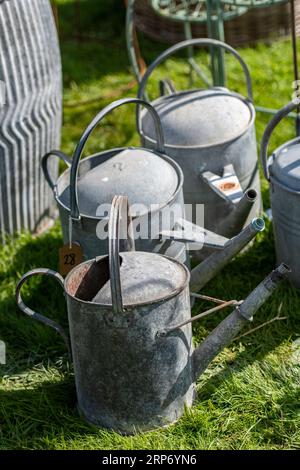 trois arrosoirs en métal vintage galvanisé rustique exposés chez un détaillant ou un centre de jardinage vendant des articles de jardin récupérés et anciens. Banque D'Images