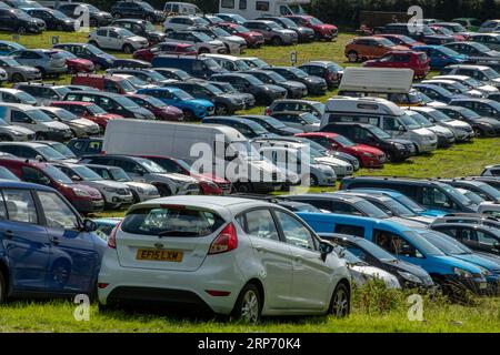 grand nombre de voitures et de véhicules garés dans un parking de campagne lors d'un grand événement estival. Banque D'Images