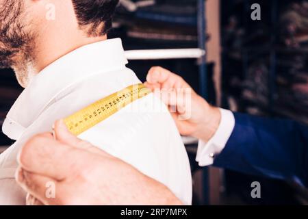 Créateur de mode prenant la mesure de son client s dos avec le ruban à mesurer jaune Banque D'Images