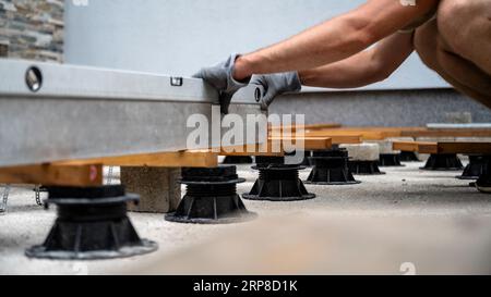 Vue à angle bas d'un homme dans des gants de protection, travailleur, nivelant une construction de support en bois pour une terrasse avec un niveau à bulle dans un projet de bricolage. Banque D'Images
