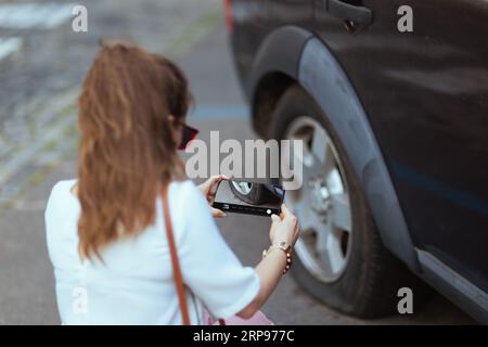 Accident de voiture. Gros plan sur femme de voyageur dans la ville avec smartphone près de la voiture avec pneu crevé. Banque D'Images