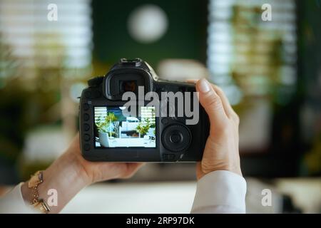 Il est temps de passer à autre chose. Gros plan sur femme agent immobilier dans le bureau vert en blouse blanche avec appareil photo reflex numérique faisant photo d'intérieur. Banque D'Images