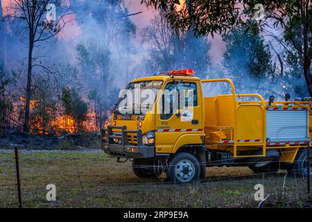 Appareil jaune Rural Fire Service avec flammes en arrière-plan gérant une brûlure contrôlée. Maryborough Queensland Australie Banque D'Images