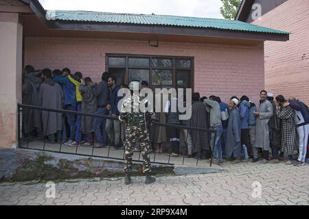 (190418) -- SRINAGAR, 18 avril 2019 (Xinhua) -- un soldat paramilitaire indien monte la garde alors que les électeurs cachemiris font la queue pour voter pendant la deuxième phase des élections générales indiennes, devant un bureau de vote dans la banlieue de la ville de Srinagar, capitale estivale du Cachemire contrôlé par l Inde, le 18 avril 2019. (Xinhua/Javed Dar) CACHEMIRE-SRINAGAR-ELECTION-SECOND PHASE PUBLICATIONxNOTxINxCHN Banque D'Images