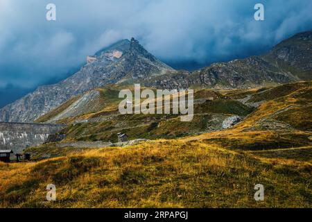 Vue sur les collines avec de l'herbe jaune et le sommet de la montagne sous ciel nuageux sur fond près du col de Nivolet dans le parc national du Gran Paradiso, Italie. Banque D'Images