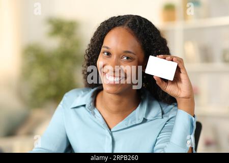 Heureuse femme noire montrant carte de crédit vierge à la maison Banque D'Images