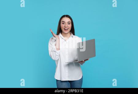 Surprise jeune femme avec ordinateur portable sur fond bleu clair Banque D'Images