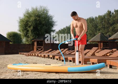 Homme pompant la planche de SUP sur la rive de la rivière Banque D'Images