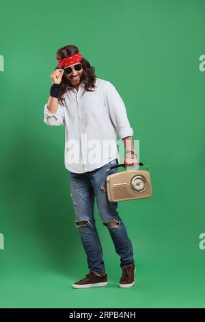 Homme hippie élégant dans des lunettes de soleil avec récepteur radio rétro sur fond vert Banque D'Images