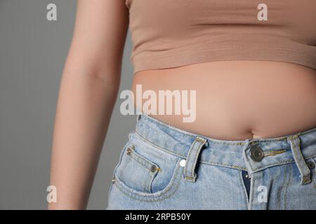 Femme en surpoids en jeans serrés sur fond gris, gros plan Banque D'Images