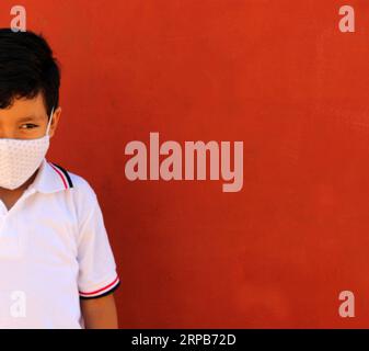 Joyeux et pensif Latino garçon de 8 ans portant une chemise blanche d'uniforme scolaire et un masque facial pour la protection contre la pandémie de Covid-19 à la rentrée scolaire Banque D'Images