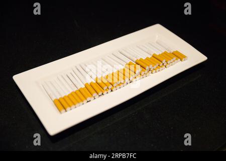 Un gros plan de cigarettes disposées sur un plateau au sommet d'une longue table en bois Banque D'Images