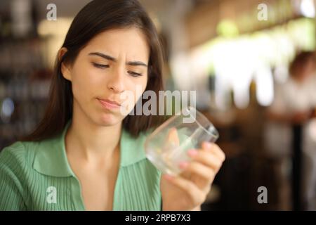 Femme déçue regardant le verre vide dans un intérieur de bar Banque D'Images