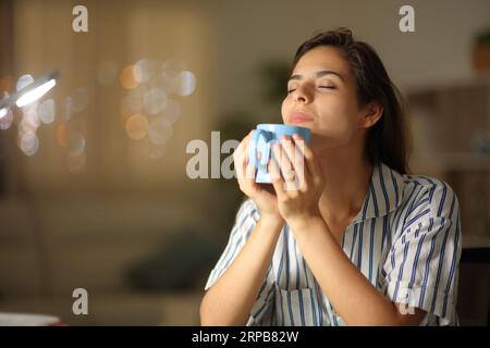 Femme sentant le café chaud assis à la maison dans la nuit Banque D'Images