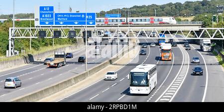 Panneaux de signalisation du statif de l'autoroute M25, pont ferroviaire et passage du train de voyageurs de Greater Anglia, au-dessus de la sortie 28 de la route pour A12 Brentwood Essex, Angleterre, Royaume-Uni Banque D'Images