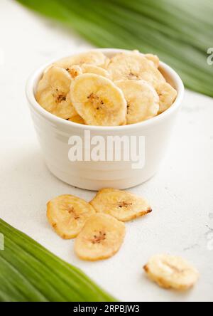 Croustilles de banane séchées jaune collation dans une assiette de bol en verre sur un tableau lumineux. Banque D'Images