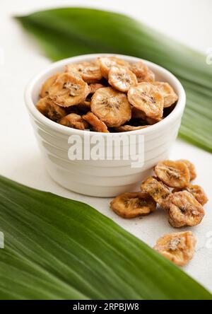 Tranches de banane fraîches et biologiques séchées dans un bol en verre avec une feuille verte. Banque D'Images