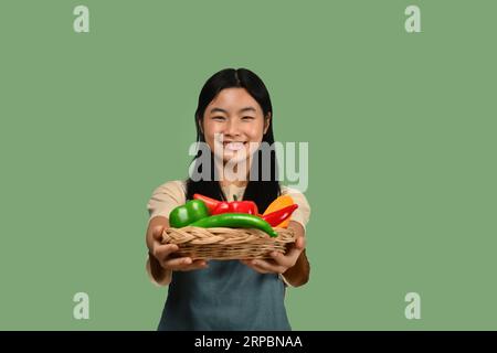 Jolie adolescente asiatique tenant le panier avec des légumes isolés sur fond vert. Concept de nourriture saine Banque D'Images