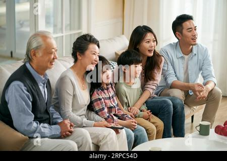 famille asiatique de trois générations assis sur le canapé à la maison regardant la télévision ensemble heureux et souriant Banque D'Images