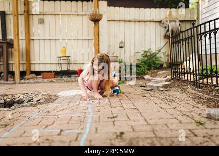 Petite fille portant le moulage de bras dessine sur le patio avec la craie de trottoir Banque D'Images