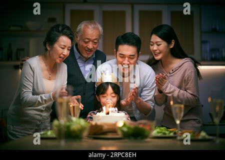 petite fille asiatique faisant un vœu alors que la famille de trois générations fête son anniversaire à la maison Banque D'Images