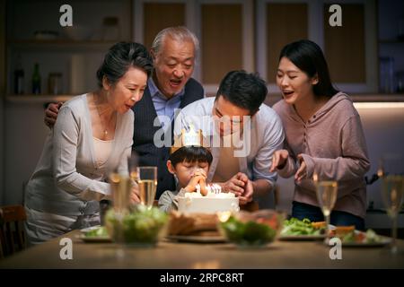 petit garçon asiatique faisant un vœu alors que la famille de trois générations fête son anniversaire à la maison Banque D'Images