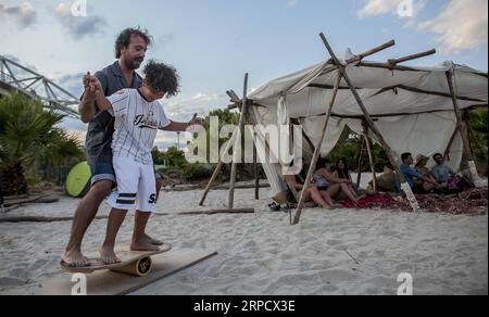 (190714) -- ATHÈNES, le 14 juillet 2019 -- Un enfant essaie des acrobaties avec l'aide d'un instructeur lors du Festival d'art du surf à Athènes, en Grèce, le 14 juillet 2019. Le Surf Art Festival est un festival de trois jours consacré à l'art de vivre et au surf. GRÈCE-ATHÈNES-SURF ART FESTIVAL PanagiotisxMoschandreou PUBLICATIONxNOTxINxCHN Banque D'Images