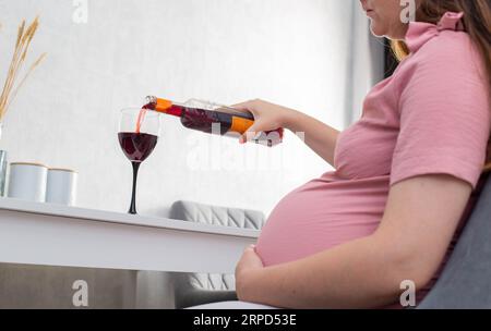 Une fille enceinte verse le vin d'une bouteille dans un verre. La notion de consommation d'alcool pendant la grossesse. Préjudice et troubles cognitifs chez l'enfant. ALC Banque D'Images