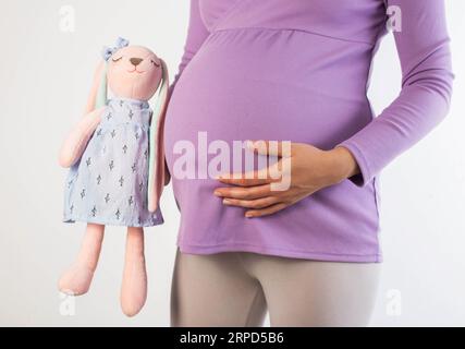 Une fille enceinte dans un chemisier violet tient un jouet doux à côté de son ventre. Concept de maternité, nouvelle vie. En prévision de la naissance du bébé, ha Banque D'Images