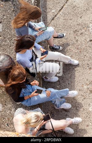 Quatre adolescentes, vues d'en haut, assises ensemble, tenant et regardant leurs téléphones portables Banque D'Images