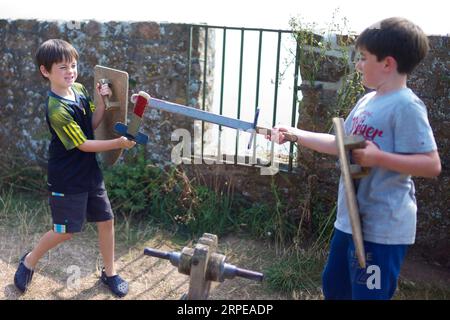 Deux jeunes garçons caucasiens prétendent se battre avec des épées et des boucliers en bois lors d'une visite d'un château historique Banque D'Images