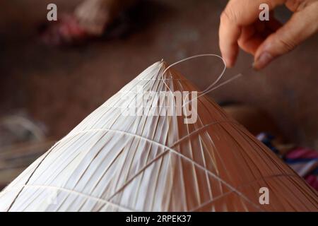 (190830) -- , 30 août 2019 -- Une femme fabrique un chapeau conique traditionnel dans le village de Chuong à la périphérie de , capitale du Vietnam le 29 août 2019. Les chapeaux coniques traditionnels du Vietnam sont principalement fabriqués à partir de feuilles de bambou et de palmier, et ils sont parmi les costumes traditionnels les plus impressionnants du pays. Les habitants du village de Chuong fabriquent des chapeaux coniques depuis environ 400 ans. Les habitants achètent des feuilles de palmier vert d'autres provinces, les séchent au soleil, repassent et blanchissent les feuilles en tranches plates. Ils utilisent ensuite de fines cordes pour fixer des couches de feuilles sur un cône fait d'anneaux de bambou, et enrober t Banque D'Images