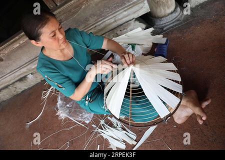 (190830) -- , 30 août 2019 -- Une femme fixe des feuilles de palmier sur un cône de bambou pour faire un chapeau conique traditionnel dans le village de Chuong à la périphérie de , capitale du Vietnam le 29 août 2019. Les chapeaux coniques traditionnels du Vietnam sont principalement fabriqués à partir de feuilles de bambou et de palmier, et ils sont parmi les costumes traditionnels les plus impressionnants du pays. Les habitants du village de Chuong fabriquent des chapeaux coniques depuis environ 400 ans. Les habitants achètent des feuilles de palmier vert d'autres provinces, les séchent au soleil, repassent et blanchissent les feuilles en tranches plates. Ils utilisent ensuite de fines cordes pour fixer des couches de feuilles sur un Banque D'Images