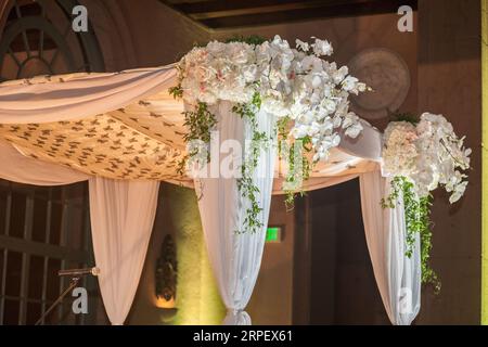 Un lieu de mariage en plein air doté d'un auvent recouvert de fleurs orné de rideaux et de rideaux pour une atmosphère romantique et élégante Banque D'Images