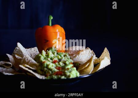 Poivron orange doux farci comme monstre avec le visage découpé sculpté dans une citrouille d'Halloween Jack O'Lantern jetant du guacamole servi avec des frites. Banque D'Images