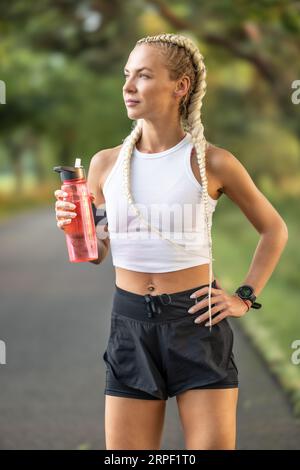 Coureuse féminine belle, tenant la bouteille d'eau et se concentrant sur la course. Banque D'Images