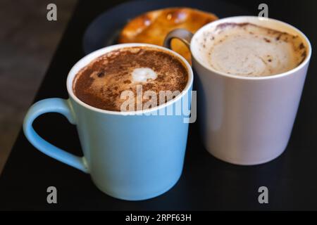 Deux tasses Cappuccino. Tasses pleines de café avec mousse de lait et cannelle en poudre se tiennent sur une table noire, photo en gros plan avec flou sélectif Banque D'Images