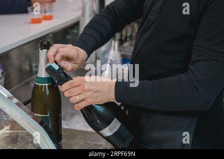 un serveur méconnaissable ouvre une bouteille de champagne à un comptoir de bar Banque D'Images