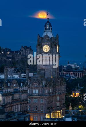 Skyline de la ville avec une super-lune bleue complète au-dessus de la tour de l'horloge Balmoral dans le ciel brumeux, Édimbourg, Écosse, Royaume-Uni Banque D'Images
