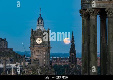 Skyline de la ville avec une super lune bleue complète au-dessus de la tour de l'horloge Balmoral, monument Scott de Calton Hill avec monument Dugald Stewart, Édimbourg, Écosse, Royaume-Uni Banque D'Images