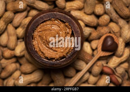 Beurre de cacahuètes crémeux et fraîchement préparé dans un bocal en bois et des tas de cacahuètes décortiquées autour Banque D'Images