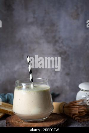 Smoothie frais et sain à la banane et à la poire, dans une tasse en verre avec un tube noir-blanc, sur un plateau en bois et un fond gris Banque D'Images