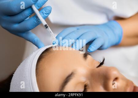 Gros plan de mains esthéticiennes injectant du botox dans le front féminin dans un salon de beauté. Effet anti vieillissement et anti rides. Concept de thérapie de rajeunissement, Banque D'Images