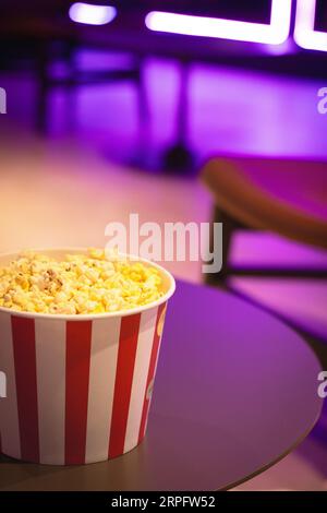 Boîte à pop-corn dans des lumières néons. Fond de pop-corn de cinéma. Concept de divertissement. Cinéma tendance. Encas cinéma. Pop-corn salé dans un seau. Restauration rapide. Banque D'Images