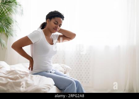 Malheureuse jeune femme noire souffrant de maux de dos dans la chambre Banque D'Images