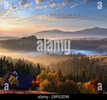 L'air. Tôt le matin, le brouillard et les premiers rayons de soleil du matin sur l'automne des pentes de montagnes des Carpates et méconnaissable farmstead (Ukraine). Banque D'Images