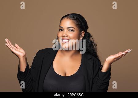 N'ai rien à dire ! Heureuse femme brésilienne écartant les mains latéralement et souriant à la caméra, posant sur fond brun Banque D'Images