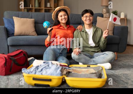 Conjoints asiatiques posant avec le drapeau du Japon et Suitcase Indoor Banque D'Images