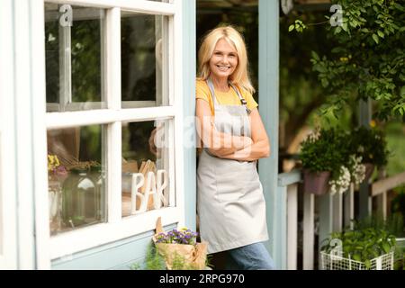 Femme mature propriétaire de petite entreprise debout sur la terrasse à son bar de campagne Banque D'Images